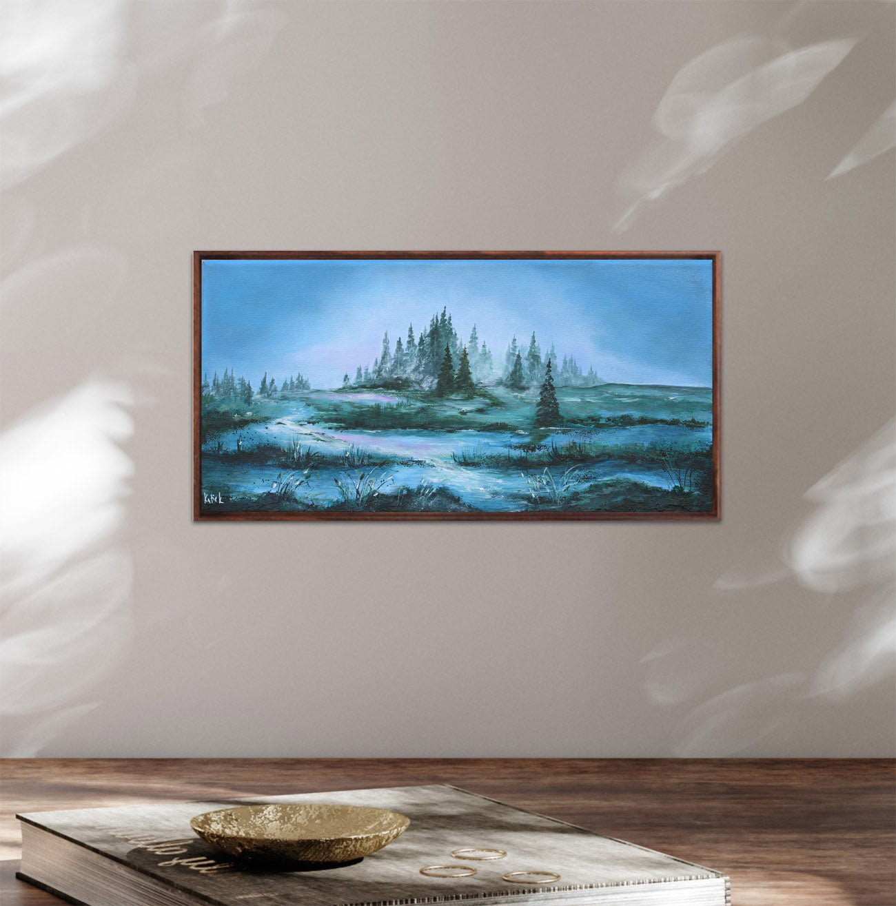 Framed painting of a landscape with trees and water on a wall.