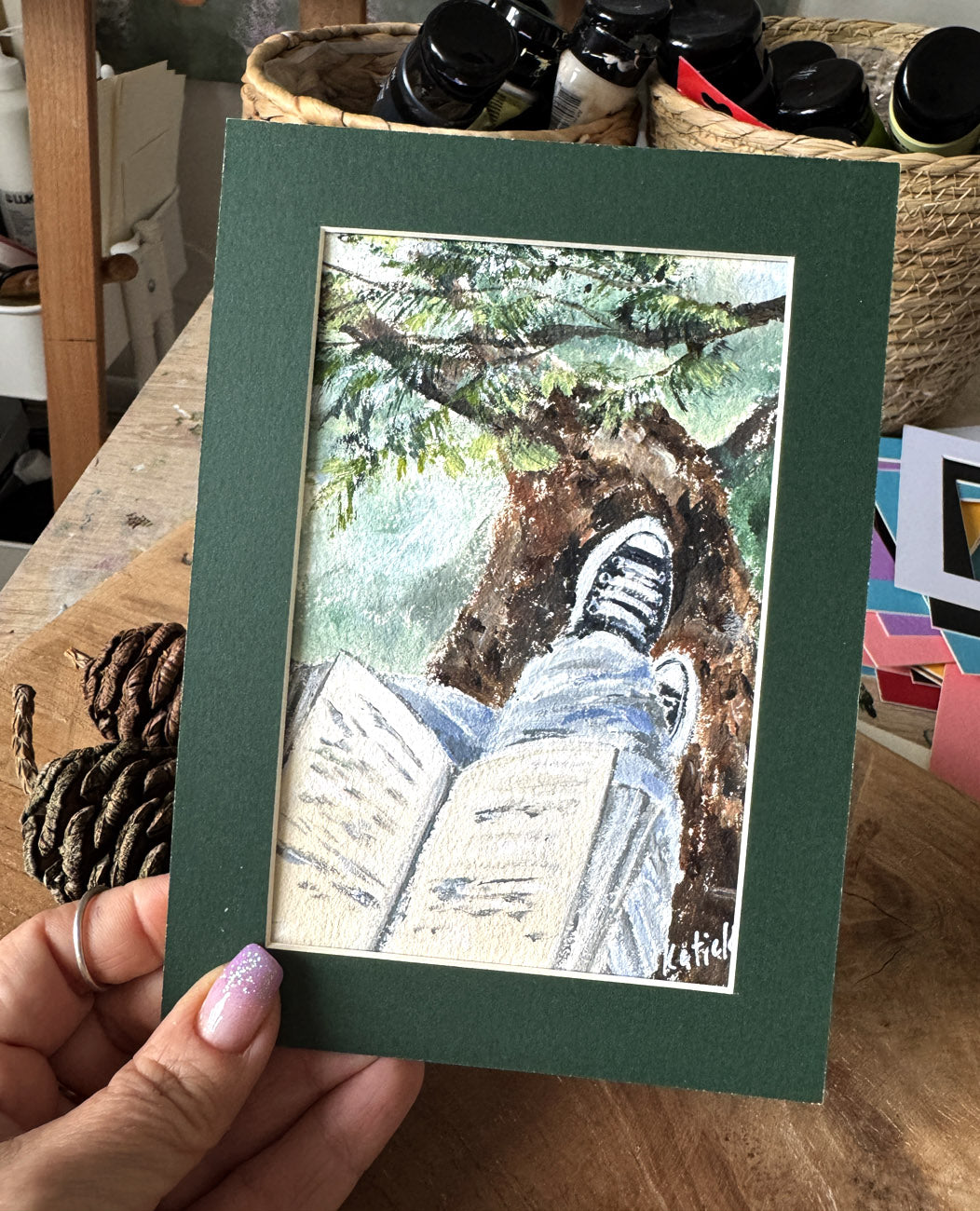 Artistic depiction of a person sitting under a tree reading a book, framed with a green border.