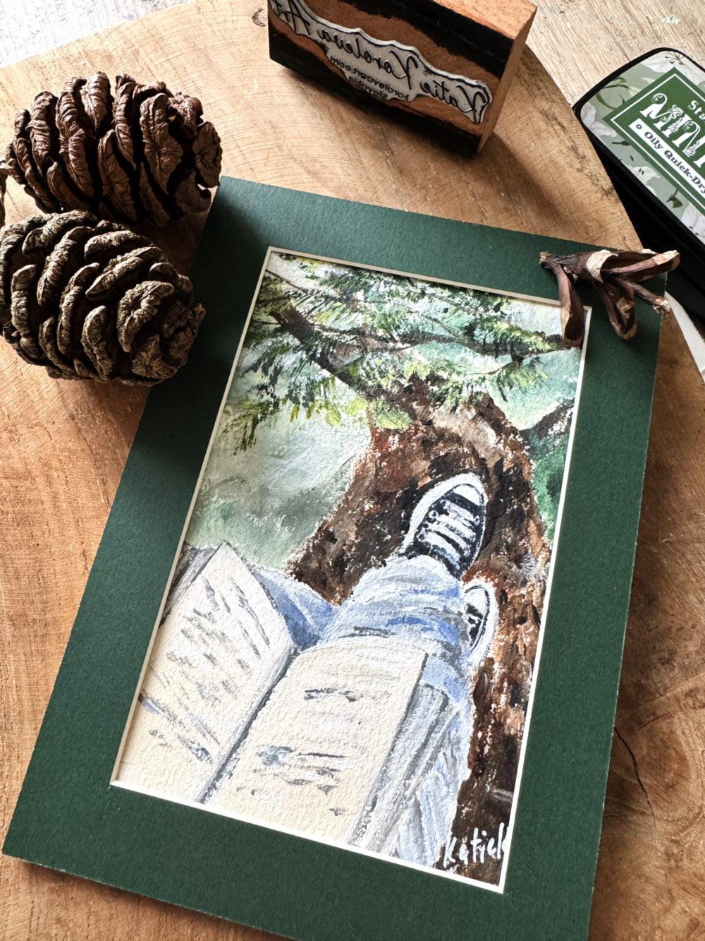 Miniature painting of a person reading a book on a tree branch with sneakers, peaceful forest art in passe-partout mat.