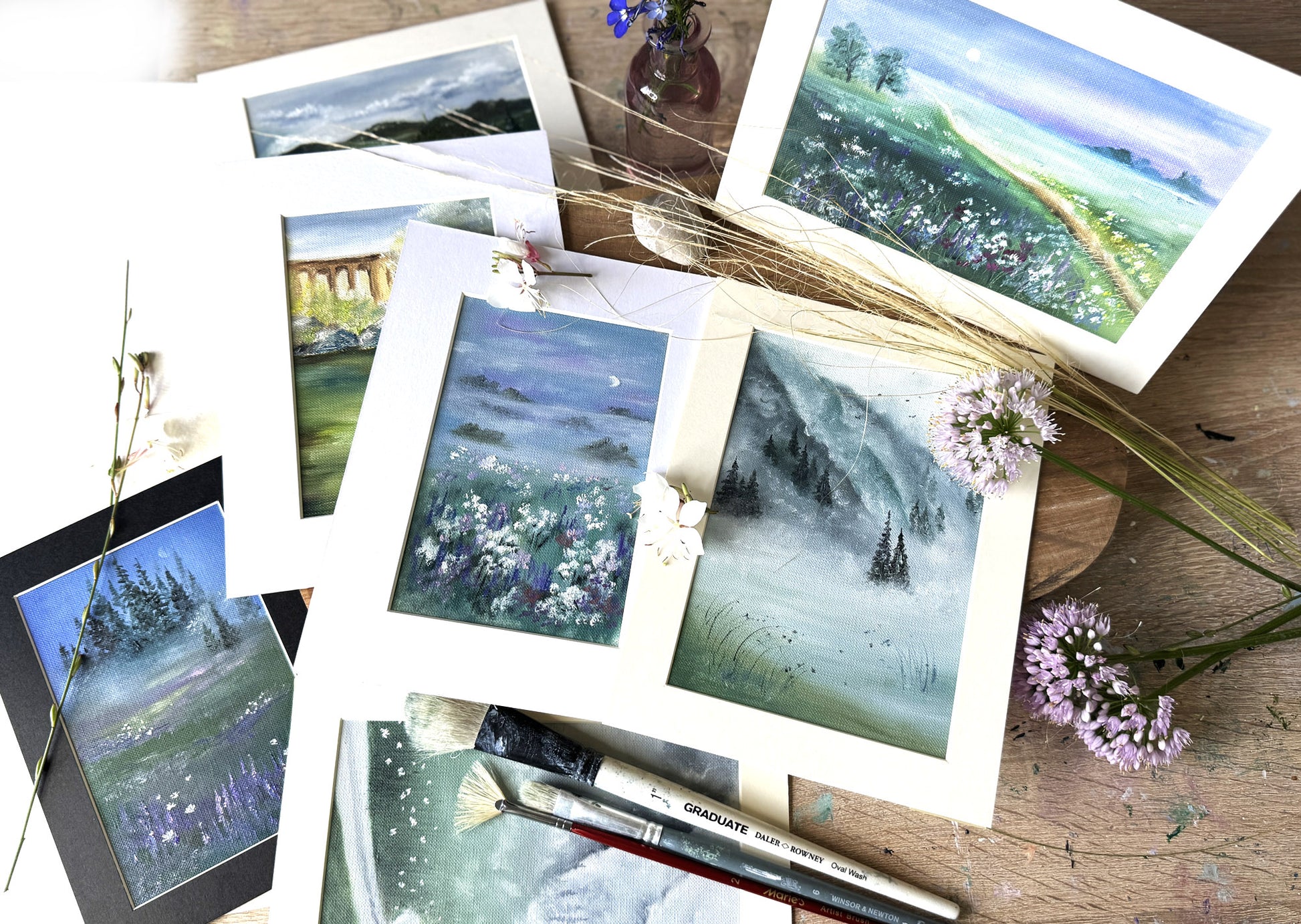 Gallery wall Collection of framed landscape paintings with flowers and brushes.