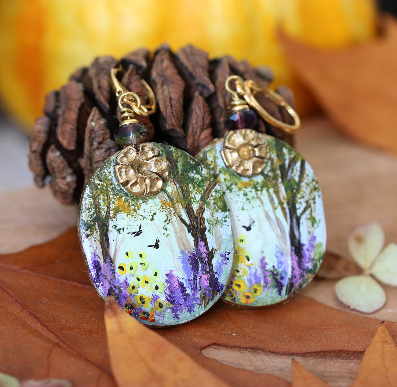 Hand painted art earrings by Katie Koroleva with wildflowers and forest landscape