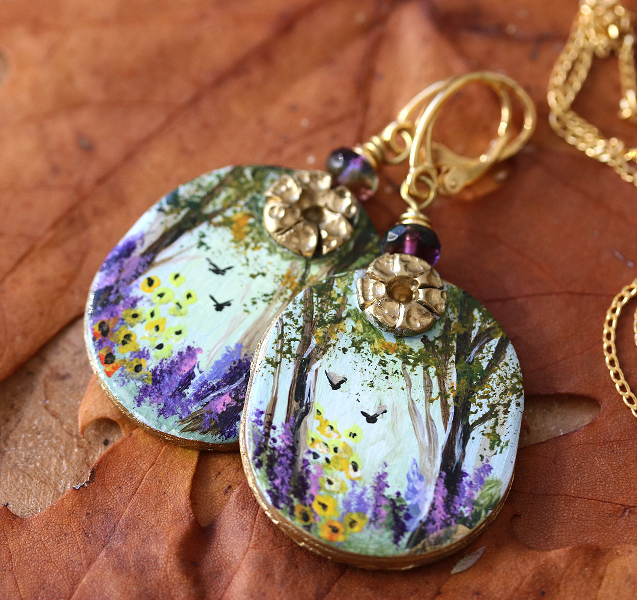 Hand painted art earrings by Katie Koroleva with wildflowers and forest landscape