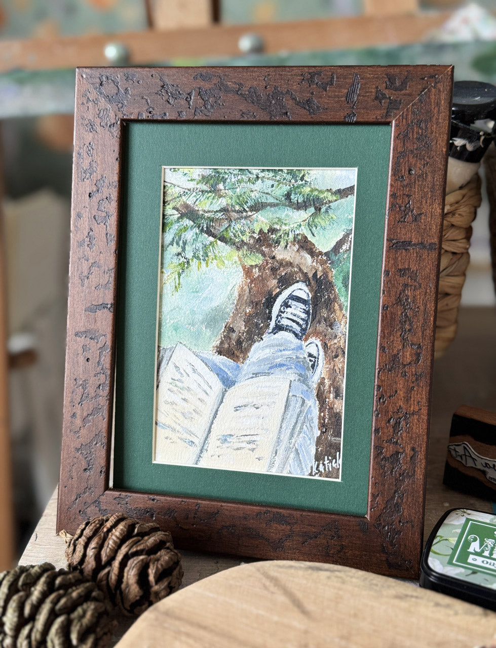 Framed artwork of a person reading under a tree with a green background