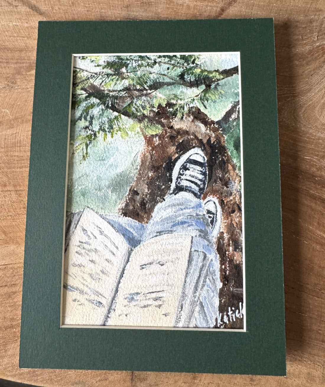 Miniature painting of a person reading a book on a tree branch with sneakers, peaceful forest art in passe-partout mat.