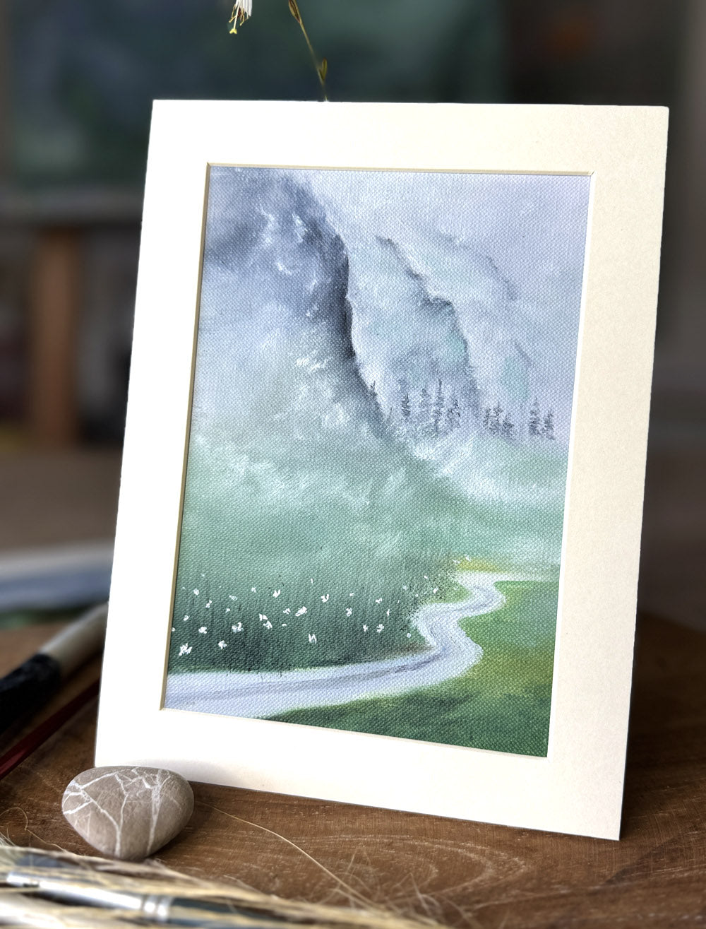 Framed artwork of a landscape with a winding road and mountains on a wooden surface.
