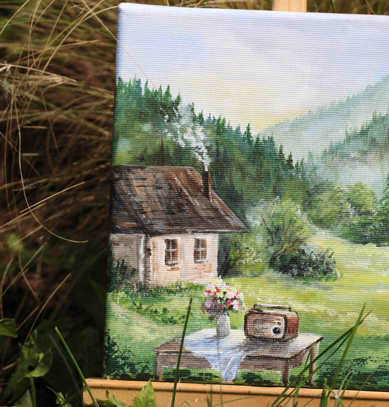Painting of a cabin in the woods with a table and radio, surrounded by nature.