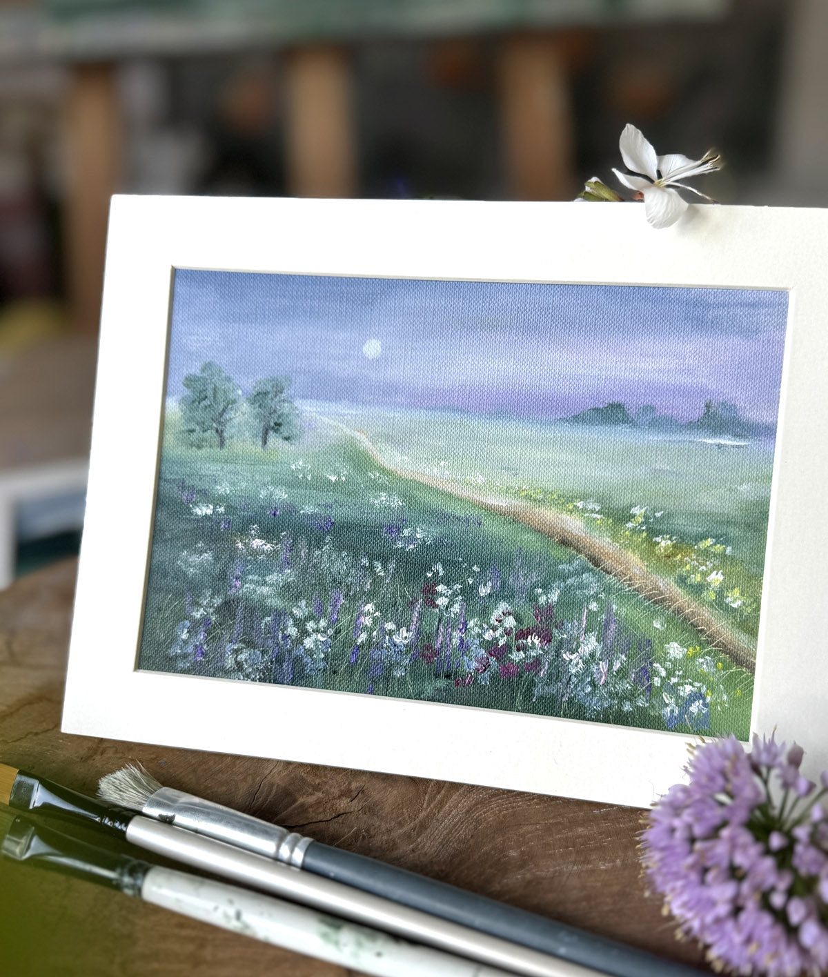 Painting of a landscape with a path and flowers on a wooden surface with paintbrushes.