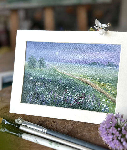 Painting of a landscape with a path and flowers on a wooden surface with paintbrushes.
