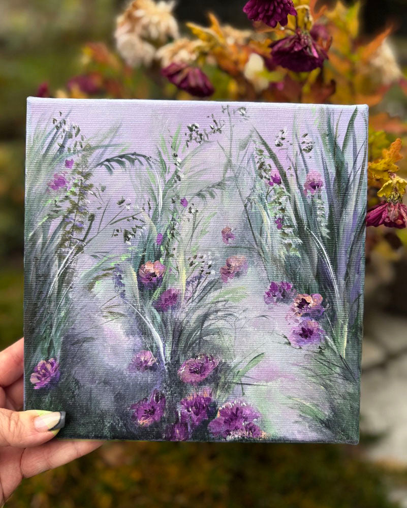 Hand holding a small painting of purple flowers and green leaves