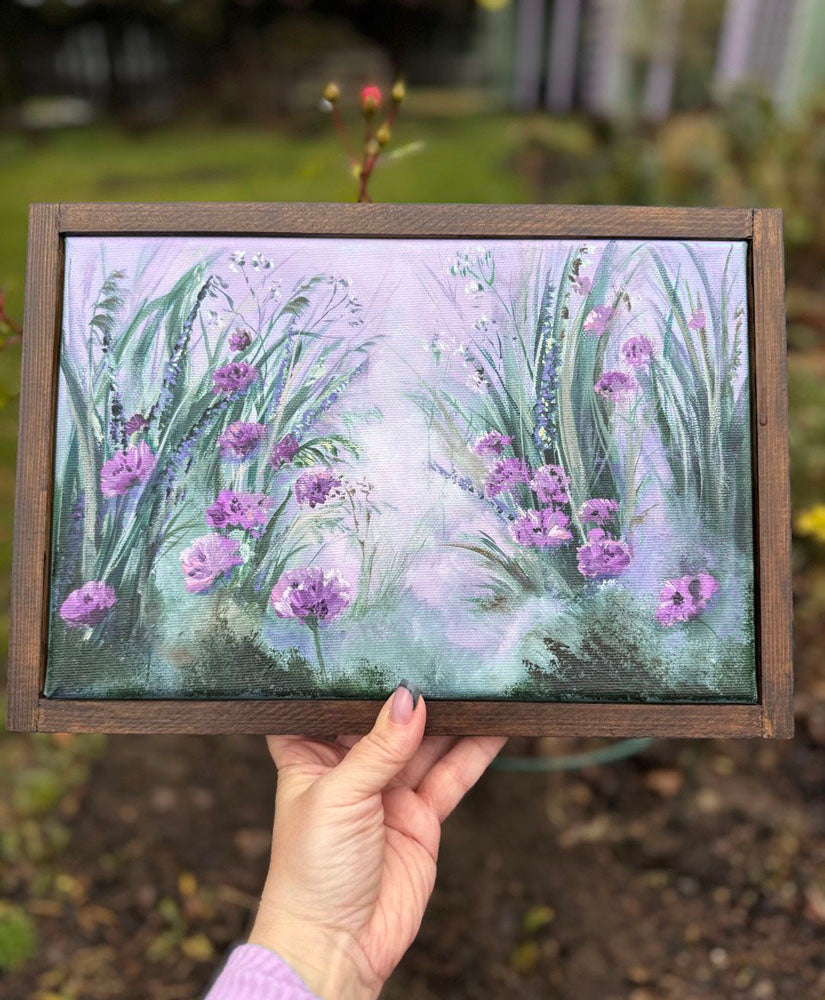 Framed artwork of purple flowers held by a hand outdoors.