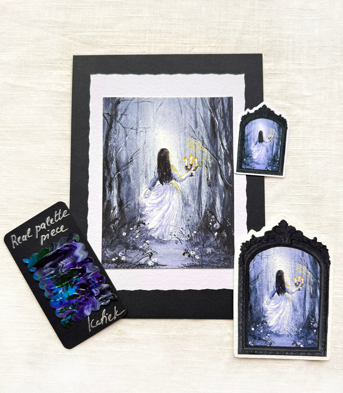 A framed art print and matching decorative pieces featuring a painted scene of a woman in a white dress standing in a misty dark blue-gray forest holding a glowing yellow lantern.