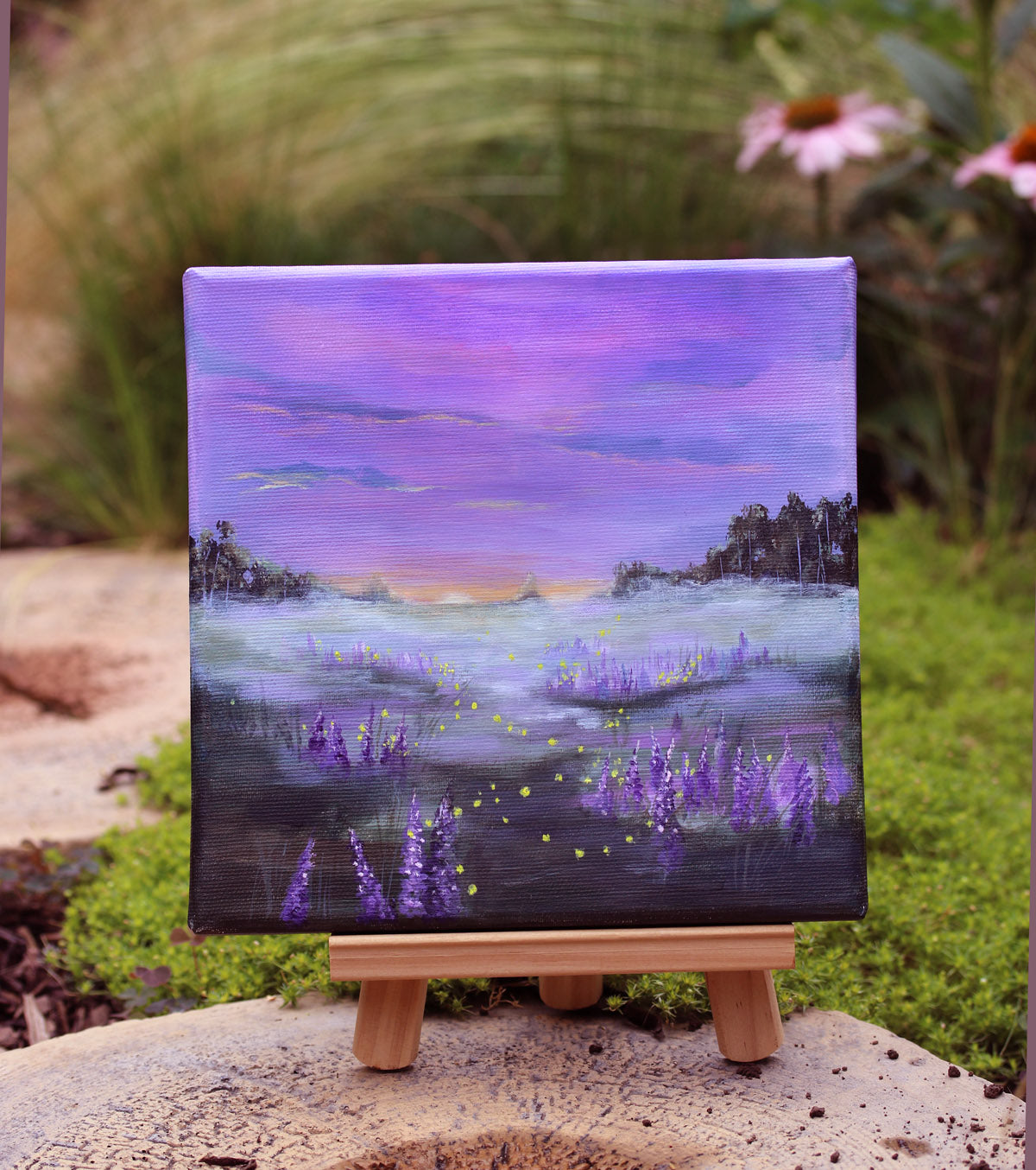A painting of a misty meadow at dusk with fireflies, with purple and lavender flowers in the foreground, dark tree silhouettes on both sides, and a pink, purple, and blue sky above.