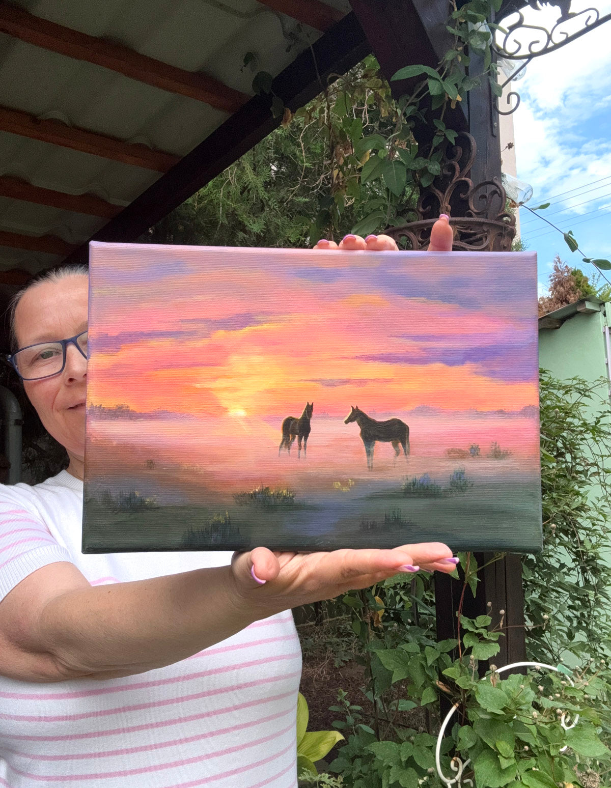 A painted landscape scene showing two dark horses standing in a misty field at sunset, with a glowing orange sun and pink, purple, and blue sky.