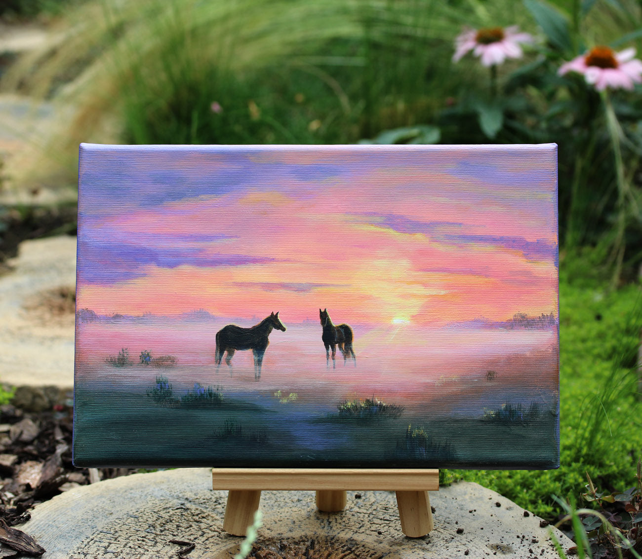 A painted landscape scene showing two dark horses standing in a misty field at sunset, with a glowing orange sun and pink, purple, and blue sky.
