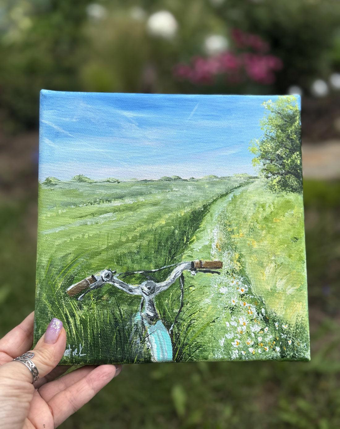 Small painting of a bicycle on a grassy field with a hand holding it.