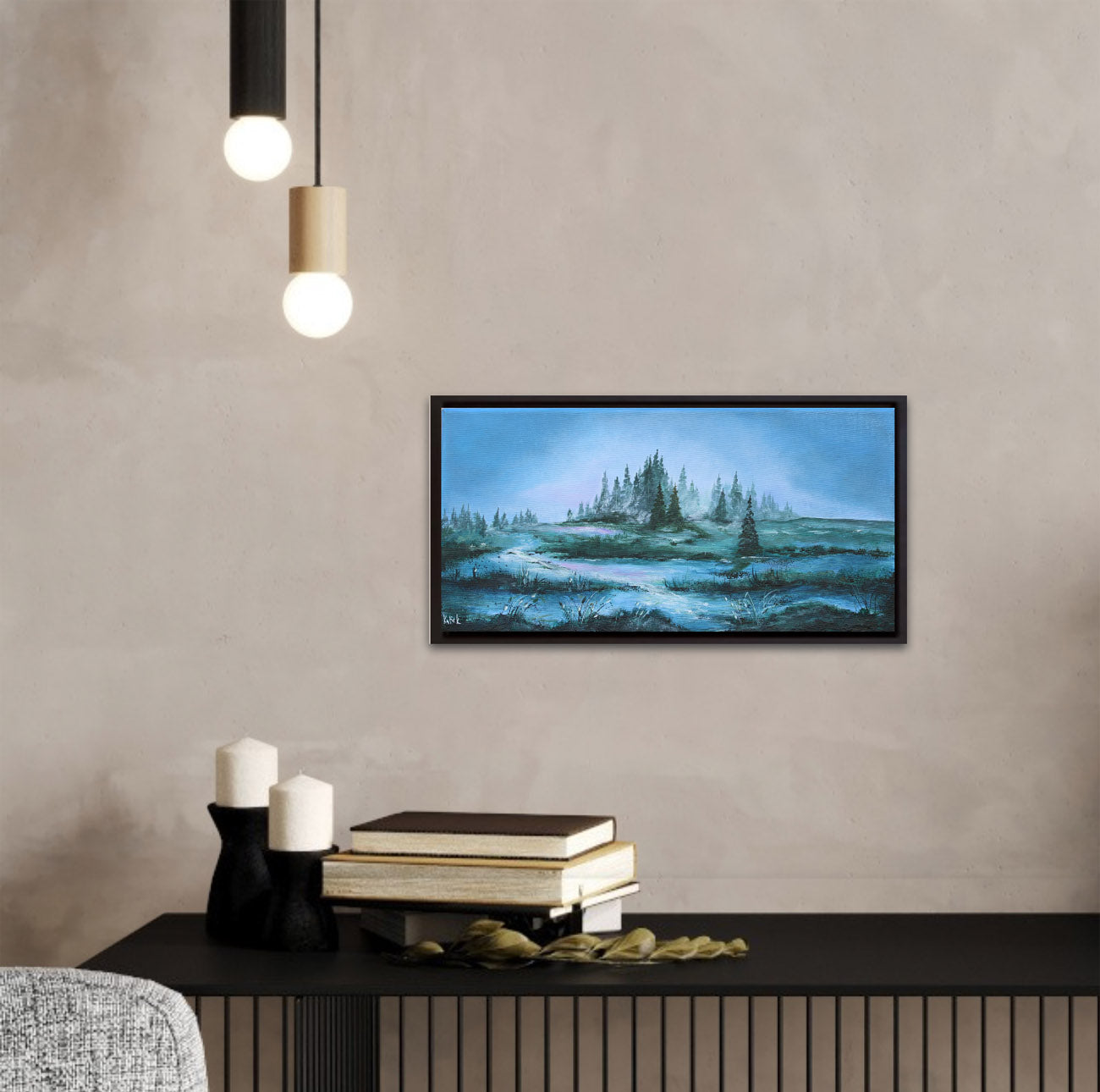 Framed landscape painting on a wall above a console table with candles and books.